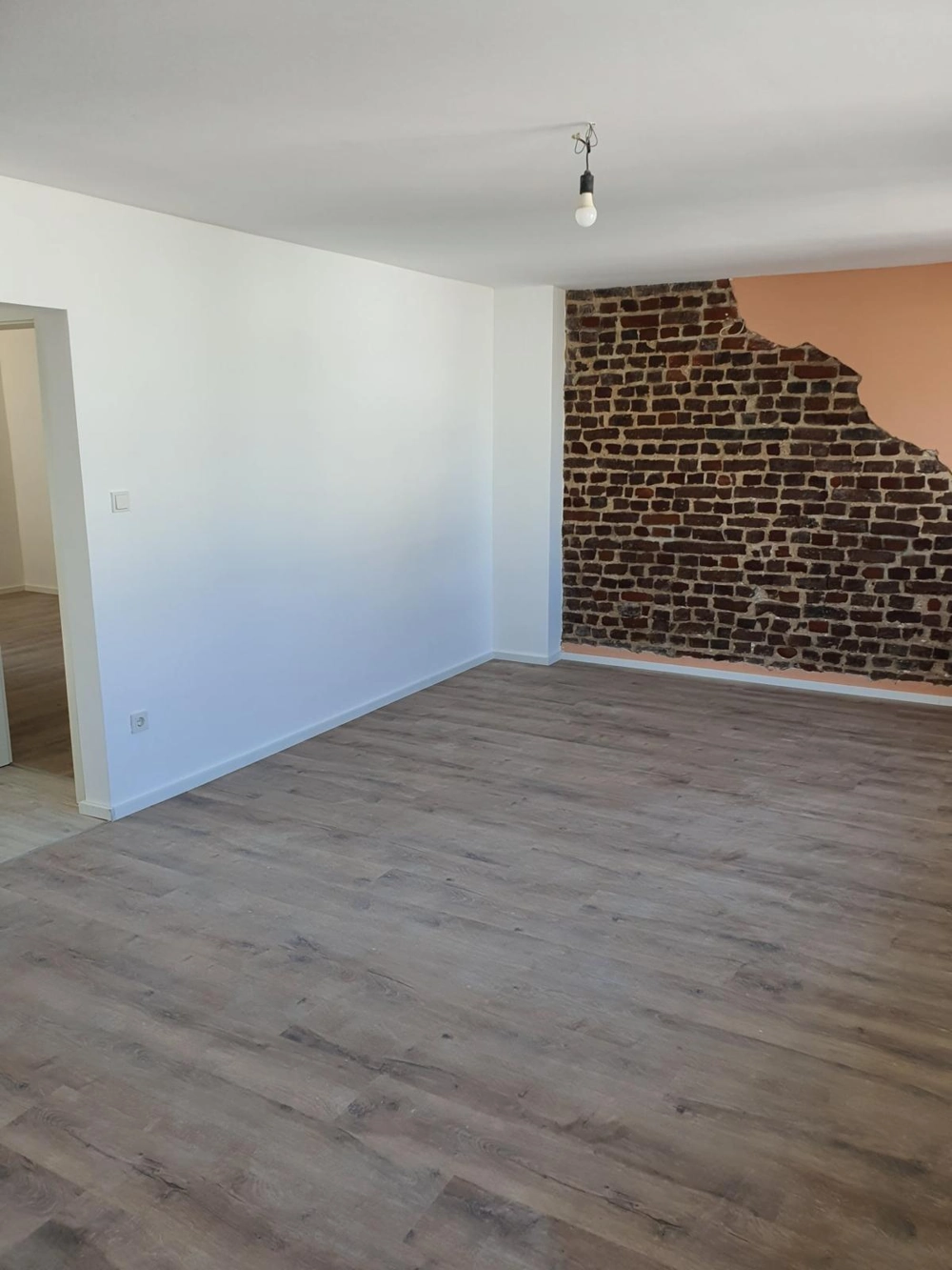 Laminat verlegen: Neuer, hellgrauer Laminatboden mit glatten weißen Wänden und rustikalen, freigelegten Backstein-Designwänden