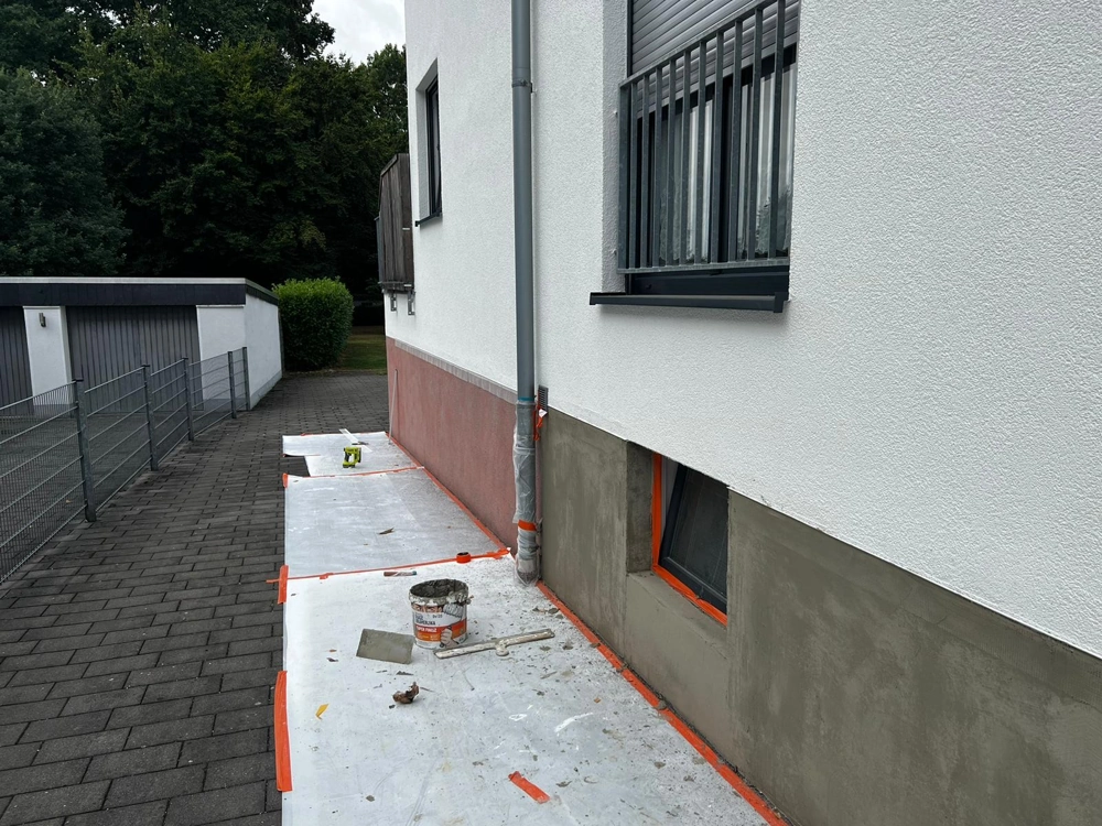 Abgeklebte Hausfassade mit Putz, Eimer und Werkzeugen für Fassadendämmung