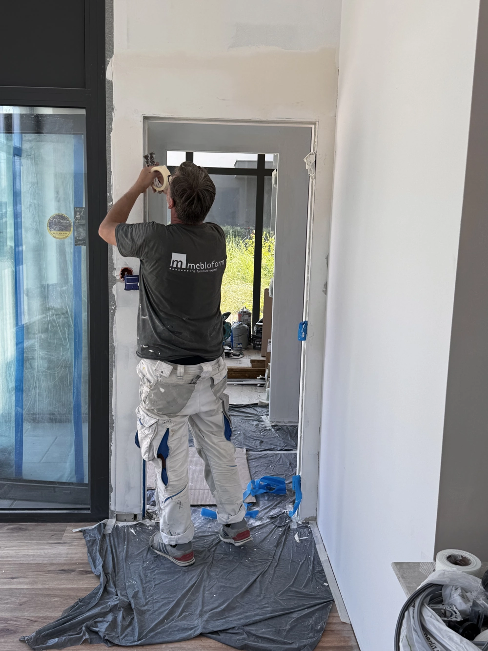 Handwerker bringt Malerkrepp am Türrahmen in renoviertem Innenraum im Rahmen von Malerarbeiten an