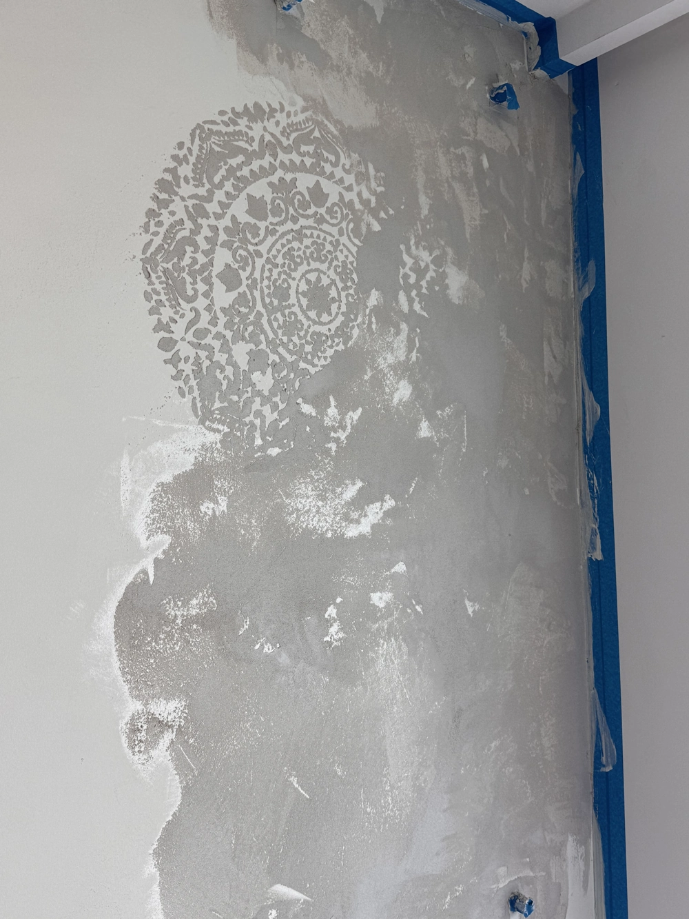 Frisch verputzte Wand mit ornamentalem Muster und blauen Abdeckband – Putzarbeiten