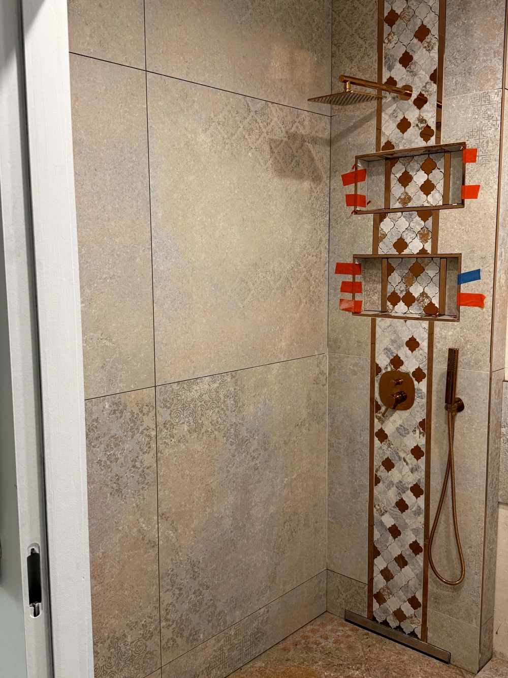Begehbare Dusche mit graubraunen Großformatfliesen, vertikalem Mosaikstreifen und Bronze-Armaturen nach Fliesen verlegen