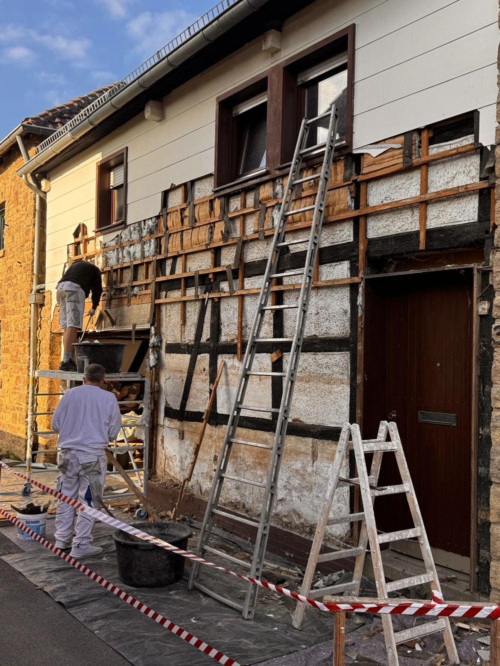 Zwei Handwerker entfernen Fassadenverkleidung an einem Wohnhaus im Rahmen der Demontage
