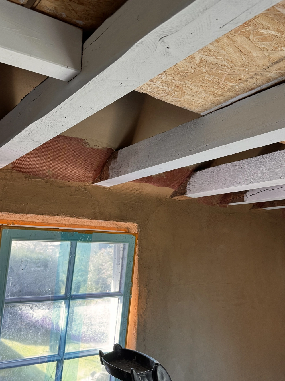 Frisch verputzte Innenwand mit Putzarbeiten an Fensterlaibung und sichtbaren Deckenbalken