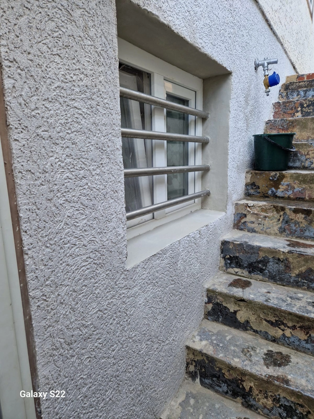 Neu verputzte Kelleraußenwand mit Kellerfenster und Metallgitter neben Betontreppe Putzarbeiten