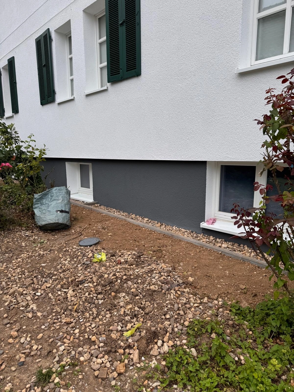 Hausfassade mit frisch verputztem Sockel, Fensterläden und Kiesbeet – Putzarbeiten