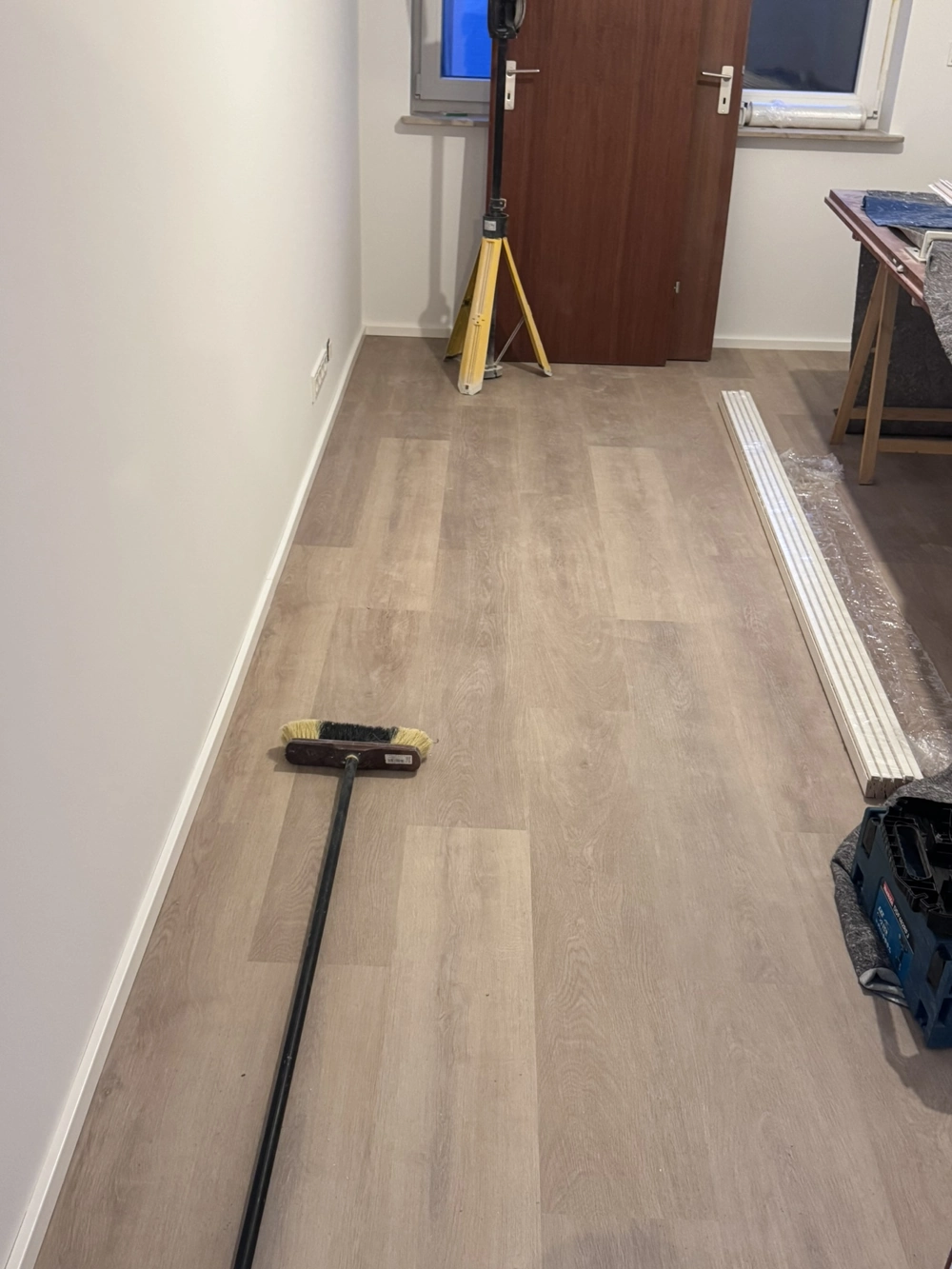 Laminat verlegen in Flur: neu verlegtes Laminat, Besen und Montagewerkzeuge