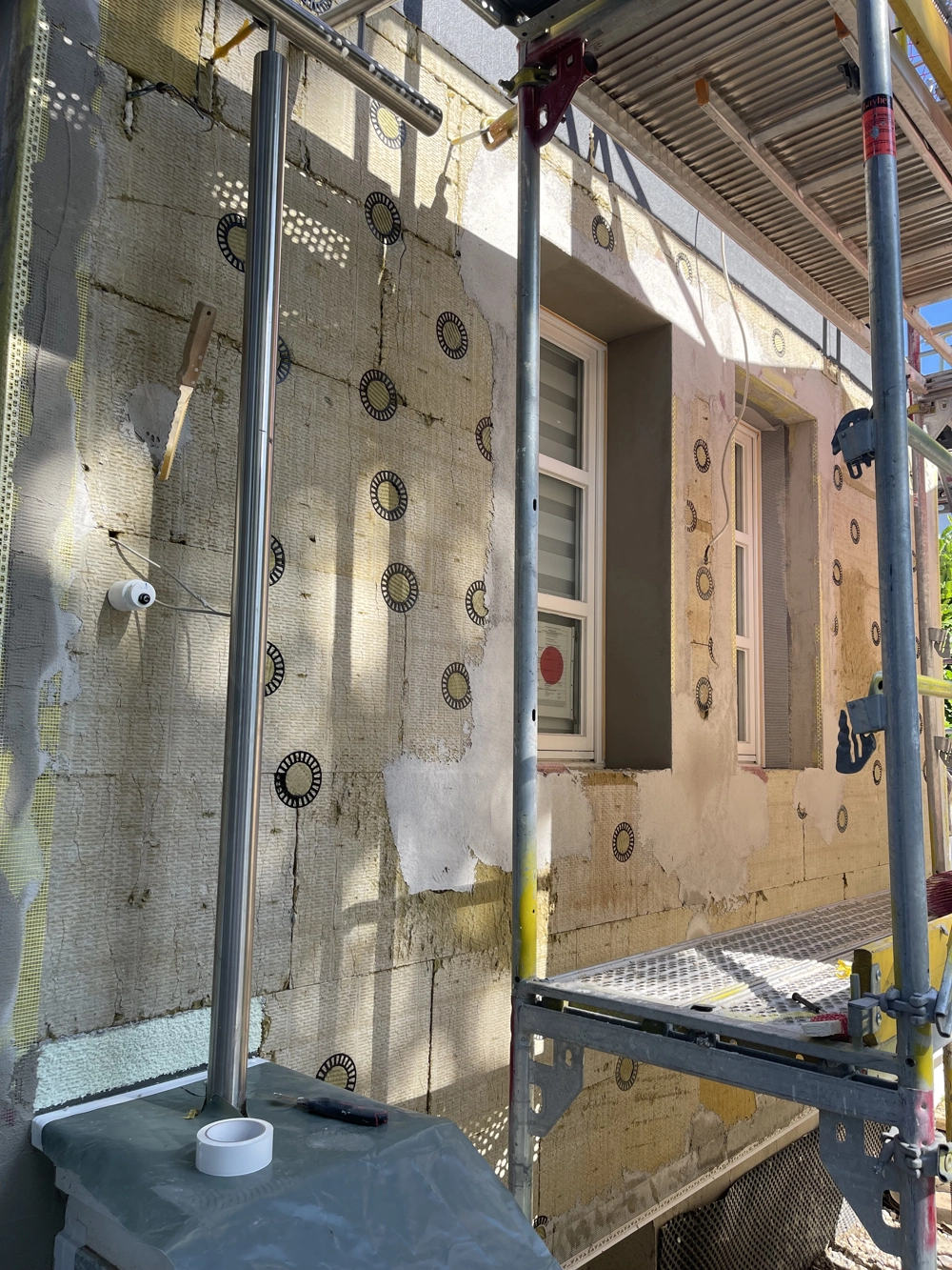 Fassadendämmung: Montage von Dämmplatten an Gebäudeaußenwand mit Gerüst und Fenstern