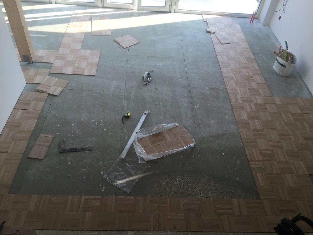 Parkett verlegen auf Estrichboden mit quadratischen Holzplatten im Innenausbau