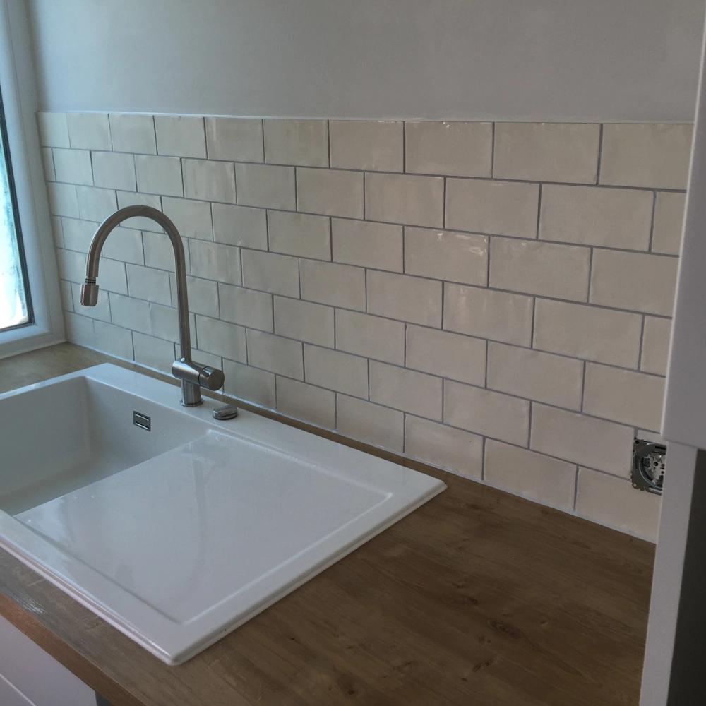 Einbau einer weißen Einbauspüle mit verchromtem Wasserhahn auf Holzarbeitsplatte und hellen Metrofliesen als Spritzschutz (Fliesen verlegen)