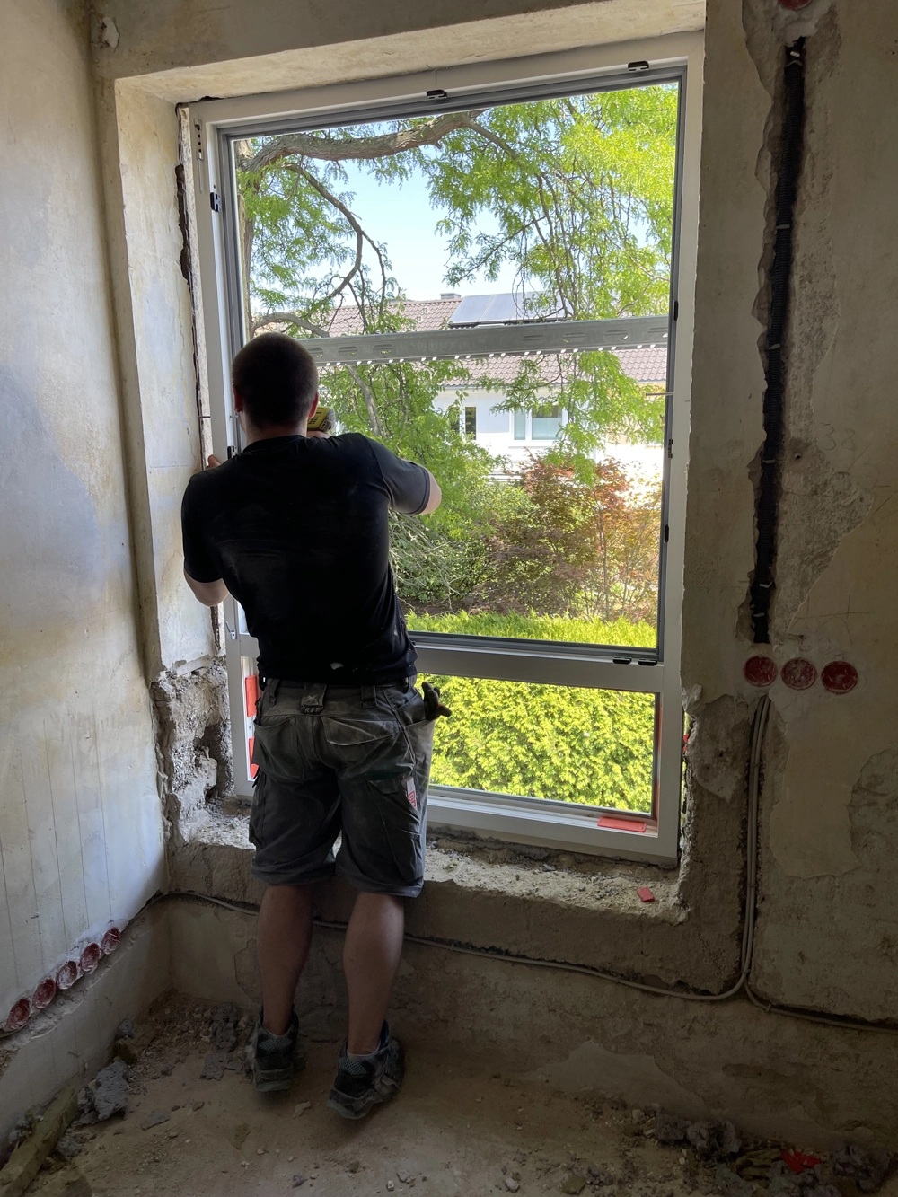 Fenstermontage: Handwerker setzt neuen Fensterrahmen in eine Rohbauöffnung im Innenbereich ein