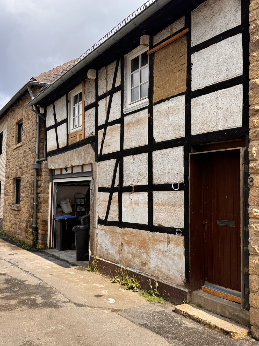 Fachwerkhausfassade mit freigelegten Holzbalken, teilentferntem Putz und Garageneinfahrt zur Altbausanierung
