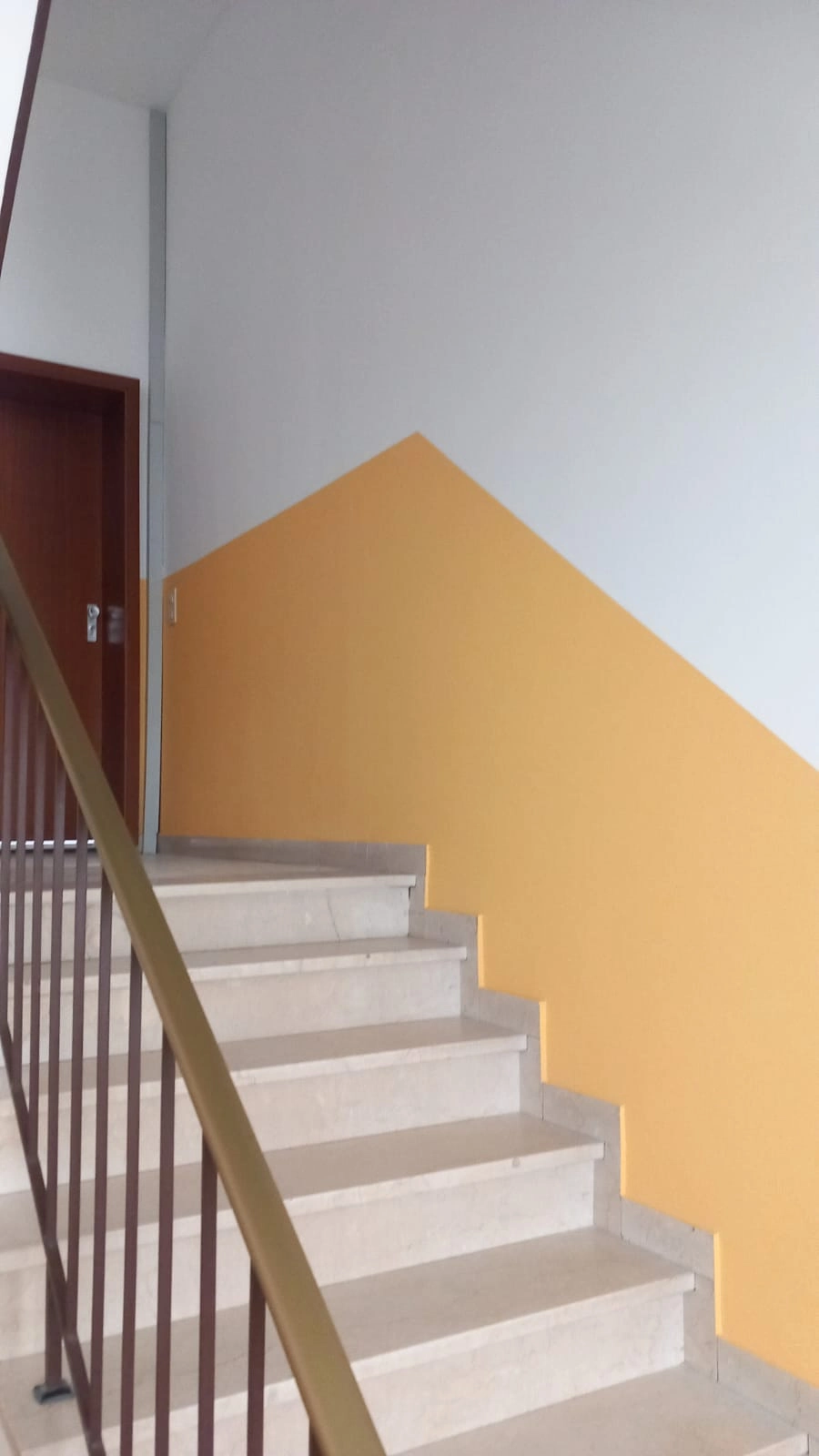 Zweifarbig gestrichene Treppenhauswand in Weiß und Gelb mit Metallgeländer und Tür – Malerarbeiten