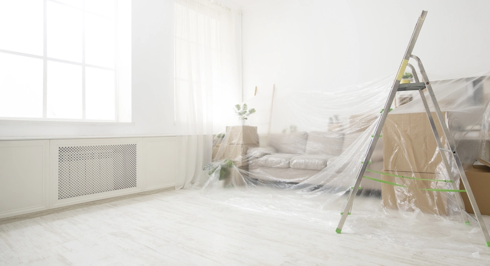 Leiter im hellen Wohnraum mit Möbeln und Boden unter Schutzfolie für Malerarbeiten