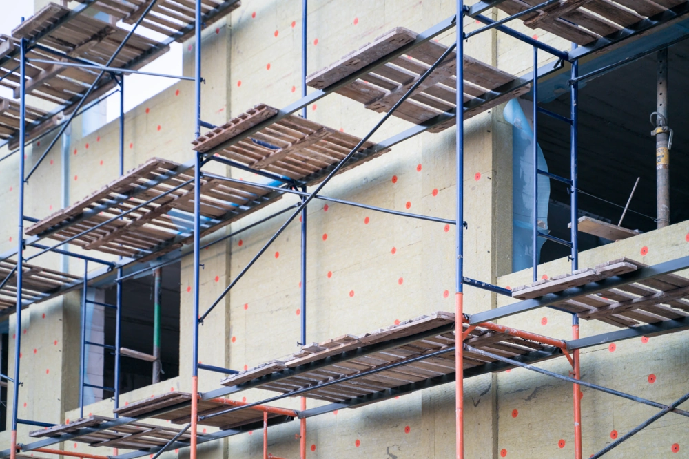 Gerüst an einer Fassade mit Wärmedämmplatten und orangefarbenen Befestigungspunkten für Fassadendämmung