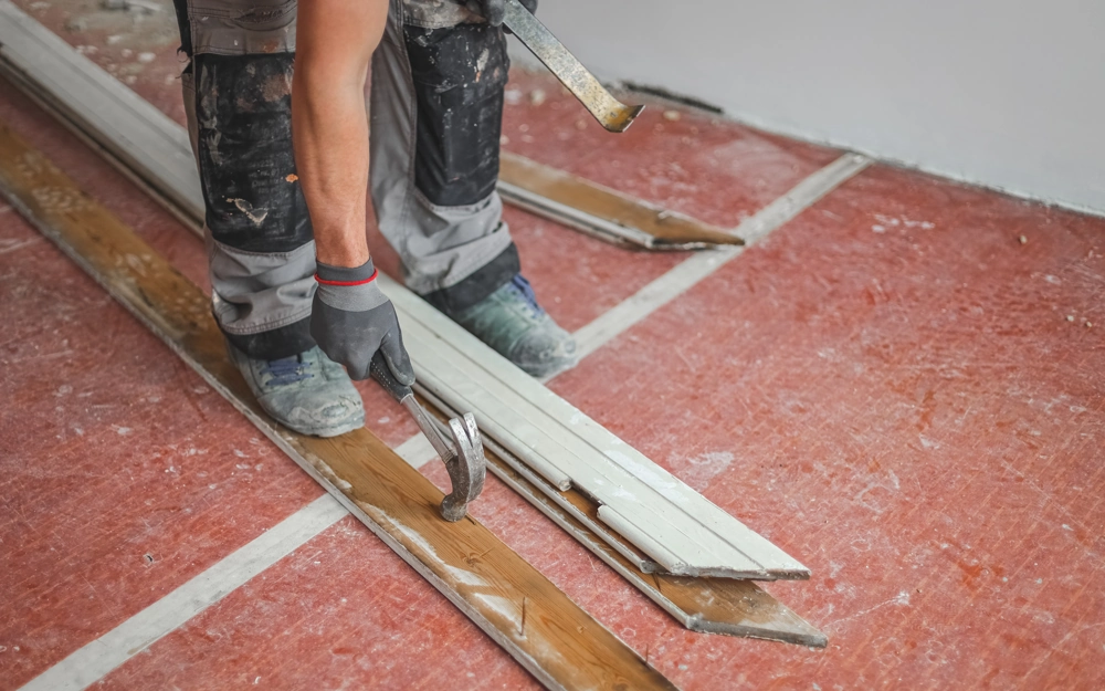 Demontage: Arbeiter entfernt alte Holzfußbodenlatten mit Brecheisen und Hammer