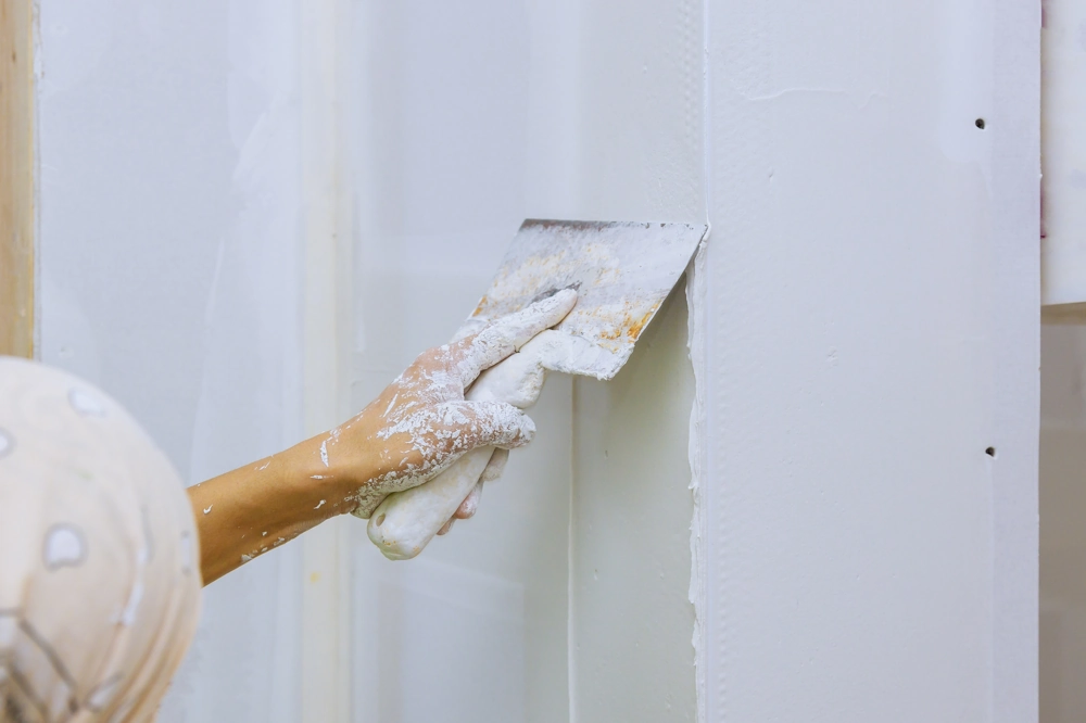 Hand mit Spachtelglätter trägt Spachtelmasse auf Gipskartonwand auf (Spachtelarbeiten)